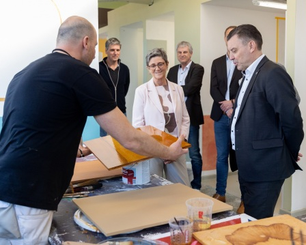 Ausbilder im Malerbereich erklärt Landrat Schröder und Geschäftsführerin Barbara Klink die Oberflächenbehandlung von Holz