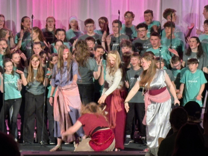 3 Junge Frauen verstoßen eine weitere Frau und schimpfen auf sie ein, im Hintergrund singt der Chor