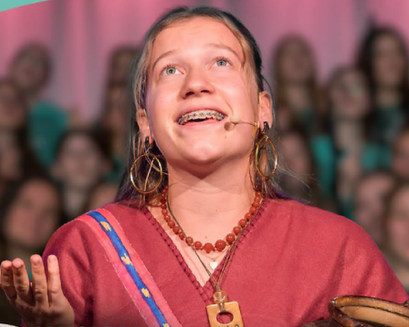 Mädchen singt mit einem Chor im Hintergrund und schaut zum Himmel