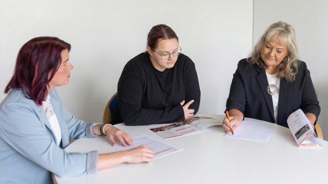 Drei Frauen sitzen an einem Tisch und besprechen gemeinsam Unterlagen in einer Beratungssituation.