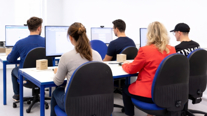 Gruppe von Personen sitzt an Computern in einem Schulungsraum und arbeitet konzentriert an Bildschirmen.