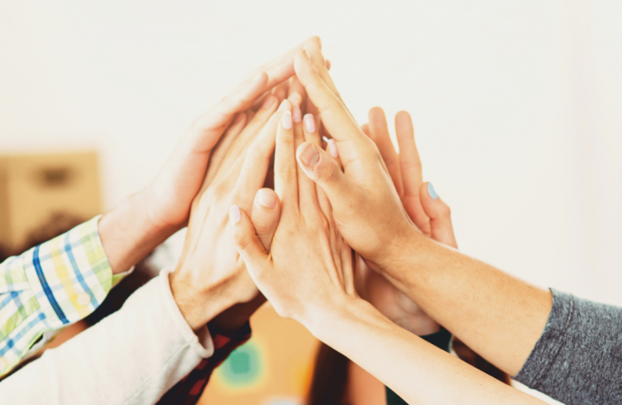 Mehrere Hände werden übereinandergelegt und symbolisieren Zusammenarbeit, Vertrauen und Gemeinschaft.