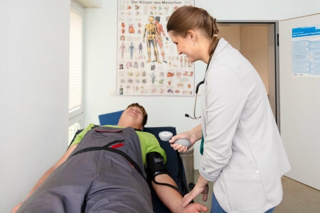 Eine medizinische Fachkraft misst den Blutdruck eines jungen Mannes, der auf einer Liege liegt.