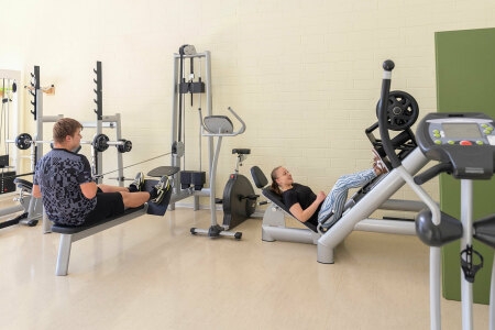 Zwei Personen trainieren an Fitnessgeräten in einem hellen Sportraum.