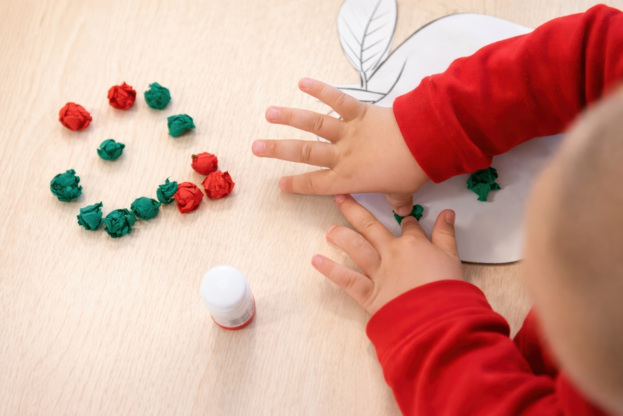 Kinderhände kleben Papierkugeln auf eine Apfel-Schablone.