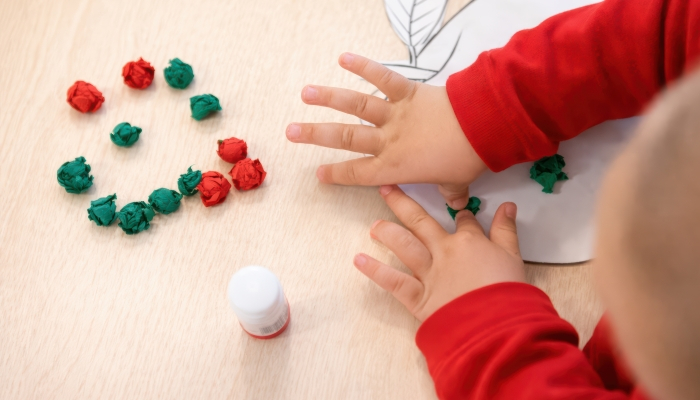 Kinderhände kleben Papierkugeln auf eine Apfel-Schablone.