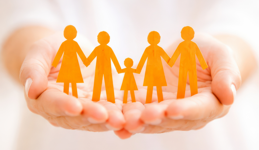 Hände halten eine stilisierte Familie aus Papierfiguren, die Zusammenhalt und Schutz symbolisiert.
