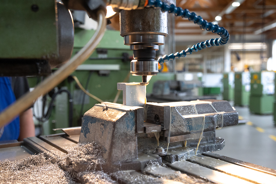 Fräsmaschine bearbeitet ein eingespanntes Metallstück in einer Werkstatt, Metallspäne und Kühlmittel sind sichtbar.