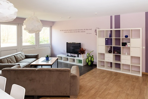 Wohnheim mit Fenstern, Sofas und einem Regal.