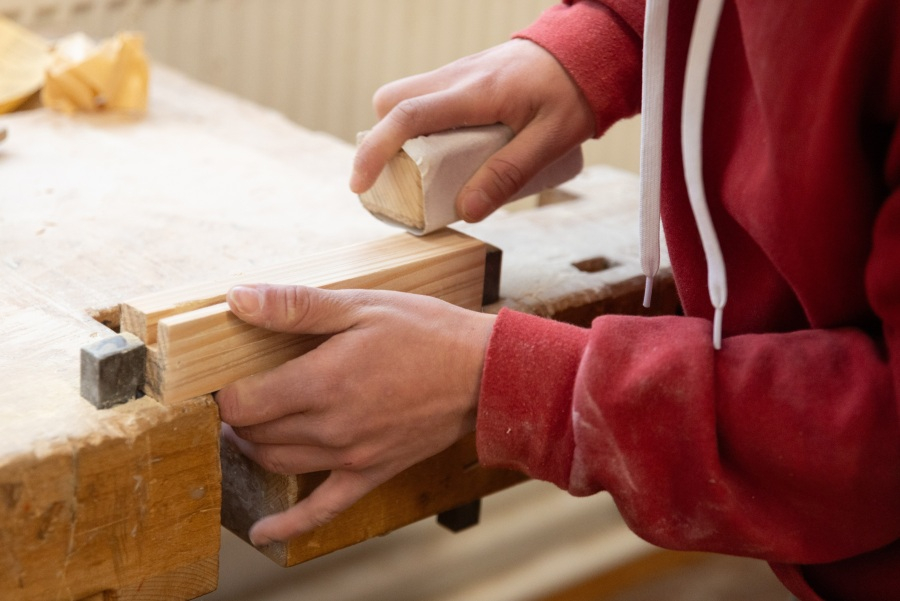 Eine Person schmirgelt ein Holzstück glatt, das in einer Werkbank eingespannt ist.