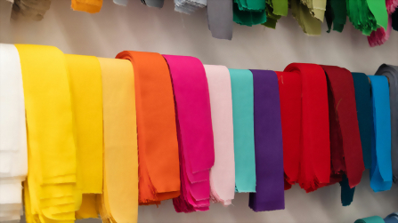 Farbig sortierte Stoffbahnen h&auml;ngen in Reihen an der Wand einer N&auml;herei und zeigen die Vielfalt der Materialien im textilen Ausbildungsbereich des Berufsbildungswerks Hettstedt.