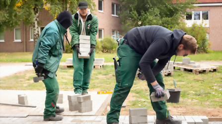 Auszubildende verlegen Pflastersteine im Bereich Garten- und Landschaftsbau des Berufsbildungswerks Hettstedt.