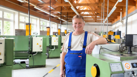 Ausbilder steht in der Metallwerkstatt zwischen Maschinen und Arbeitspl&auml;tzen.