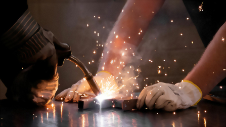 Schwei&szlig;arbeit an Metall mit Schutz&shy;handschuhen und Funkenflug in der Ausbildungswerkstatt.