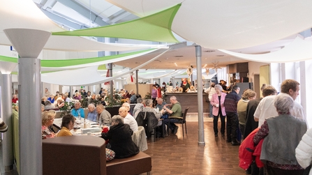 Belebte Cafeteria mit vielen Menschen, die an Tischen sitzen, essen und sich unterhalten in Hettstedt