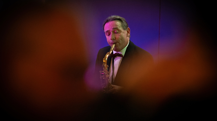 Musiker spielt Saxofon bei einer Veranstaltung im stimmungsvollen B&uuml;hnenlicht.