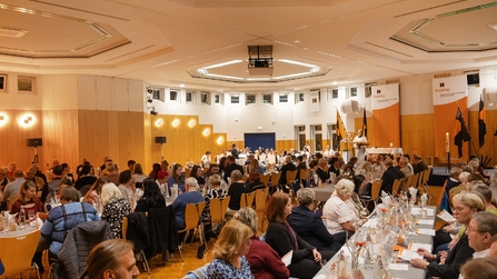viele menschen sitzen im Saal an gedeckten Tischen