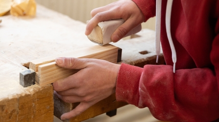 Junger Mann hobelt an Werkst&uuml;ck