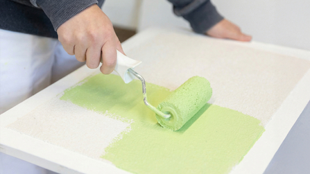 Auszubildender bemalt eine Fl&auml;che mit gr&uuml;nger Farbe